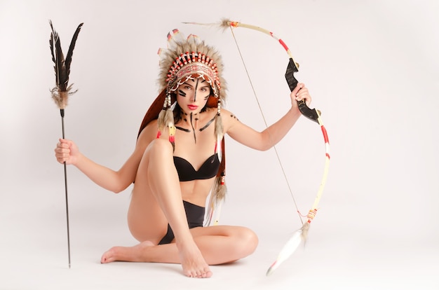 The woman in the image of indigenous peoples of america with a\
bow and arrow poses sitting on a light background