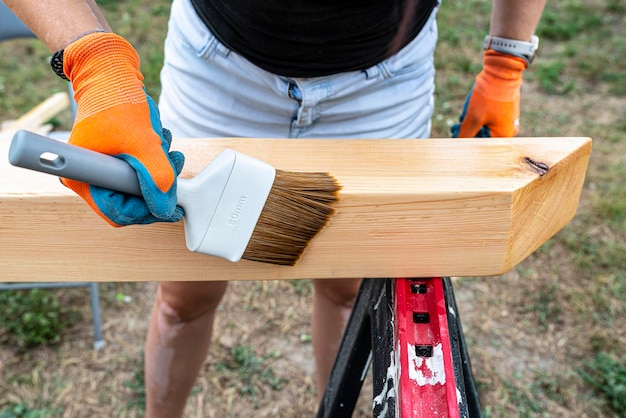 Photo the woman impregnates raw planed wooden pine beams with dimensions of 100x100mm with a colorless impregnation