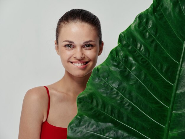Фото Женщина в красной рубашке стоит за листом пальмы на светлом фоне чистой кожи