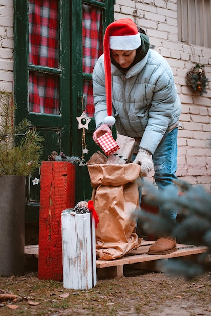 사진 산타 모자를 쓴 여자가 집 현관 앞문에서 선물 가방을 들고 있다