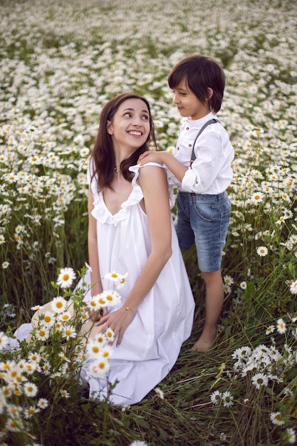 Фото Женщина в белом платье с сыном на поле ромашки при закате солнца летом