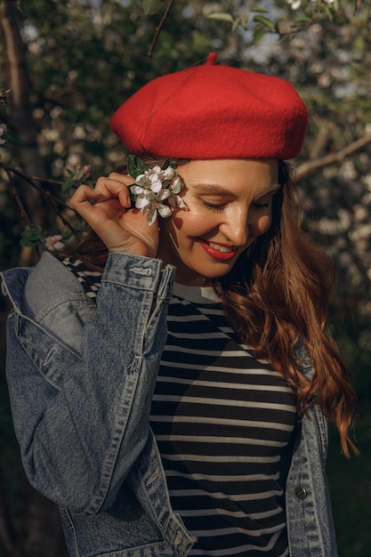 写真 ベレー帽の女性と赤い唇と波状の髪の花が咲く木の近くに立っている