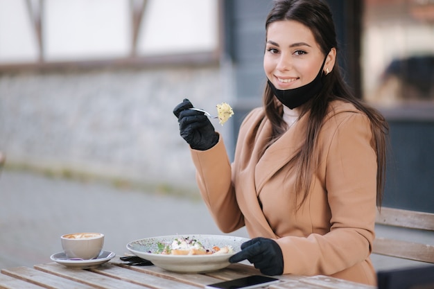 写真 カフェに座ってビーガンサラダを食べる準備をしている黒いフェイスマスクの女性。