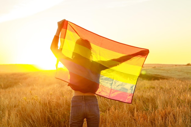 Фото Женщина в поле с радужным флагом лгбт на золотом закате вечернего солнца