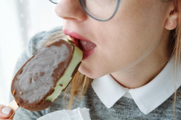 写真 メガネをかぶった女性がアイスクリームを食べて チョコレートをかぶった感性的な唇