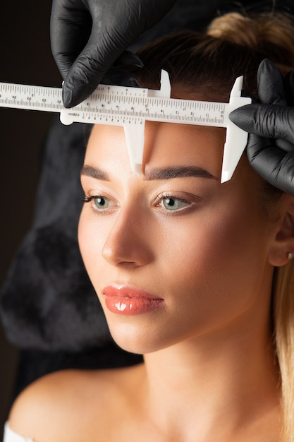 Фото Женщина в перчатках измеряет брови линейкой перед процедурой перманентного макияжа. снимок крупным планом
