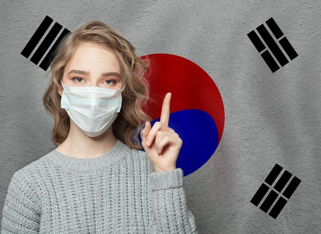 사진 의료 마스크를 착용한 여성이 한국 발을 배경으로 인플루엔자 전염병과 바이러스 보호 개념을 가리키고 있습니다.