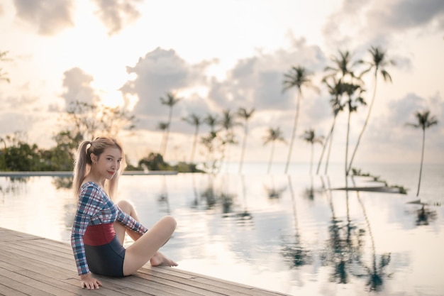 写真 スイミングプールの日没の瞬間の近くに座っているワンピース水着の女性