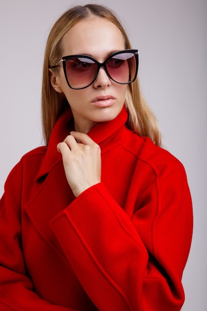 Фото Женщина в красном осеннем пальто стильные солнцезащитные очки позирует на белом фоне студия выстрел стройная фигура