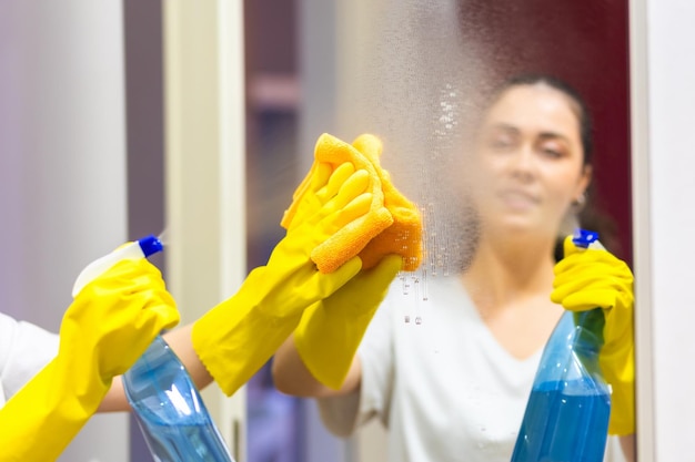 写真 ゴム製の手袋をかぶった女性がクリーナーをスプレーしガラスをラップで拭く肩から見るクリーニングサービスと家事