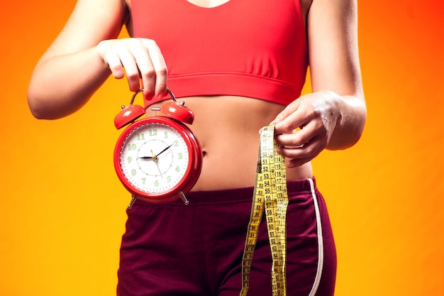 Женщина в спортивной одежде, держа будильник и метр. время fintess и концепция диеты