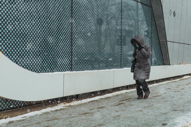 写真 雪の降る冬の路上でフードをかぶった女性