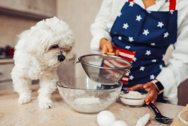 写真 台所の女性が犬と一緒に小麦粉をふるいにかける