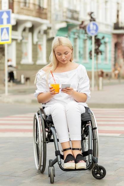 写真 飲み物を飲みながらスマートフォンを使用して車椅子の女性