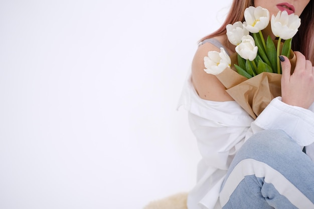 写真 白いシャツを着た女性が座って白いチューリップの花束を抱きしめている