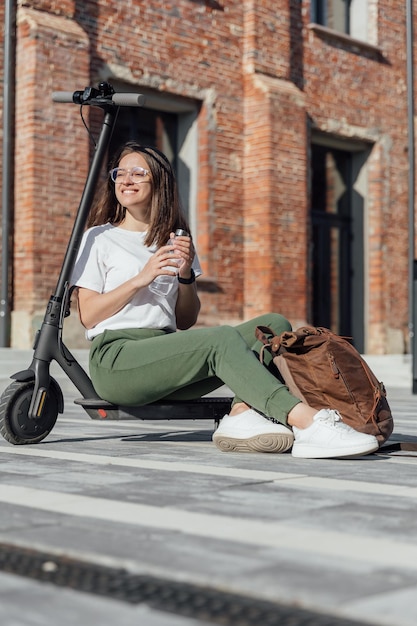 写真 電気スクーターに座っている白いスニーカーと革のバックパックの女性