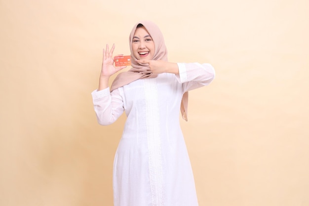 woman indonesia mature wearing a hijab smiles cheerfully holding a debit credit card in her hand and