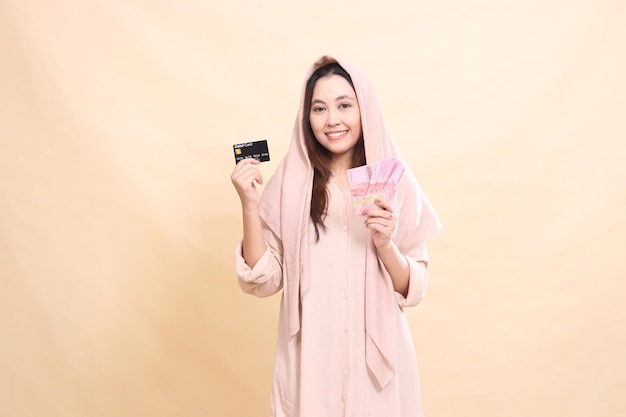 インドネシアの女性はデビットカードを掲げてルピア・モンを持って優雅に笑顔を浮かべています