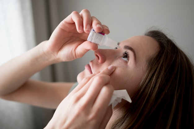 Woman indoors using  eye drops