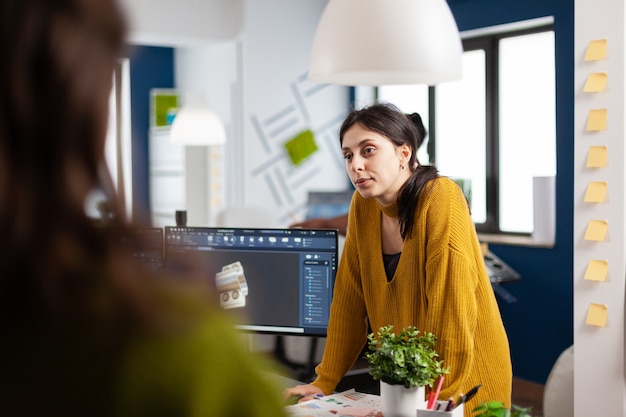 Photo woman industrial designer discussing with colleague standing at desk while working in cad program, designing 3d prototype of components