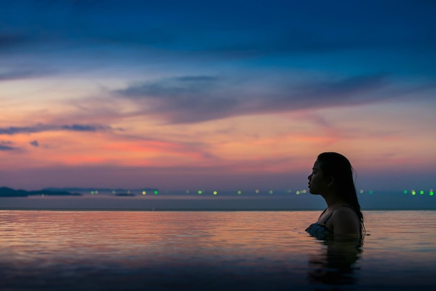Женщина в бесконечном бассейне во время захода солнца