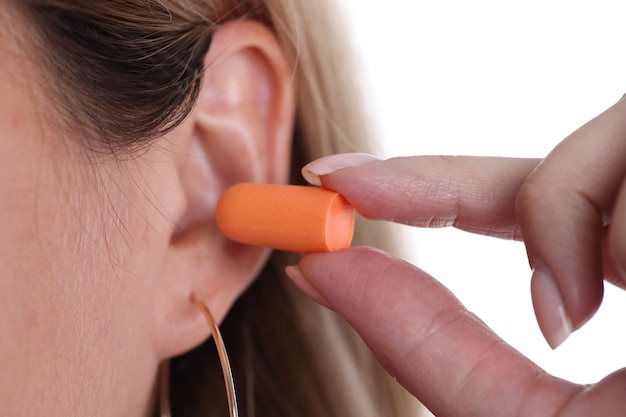 Woman inserts orange earplugs into ears types of sleep ear plugs concept