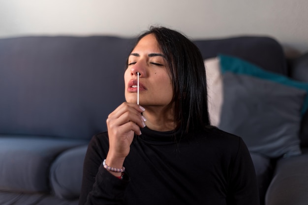 Woman inserts swab into nose at home.