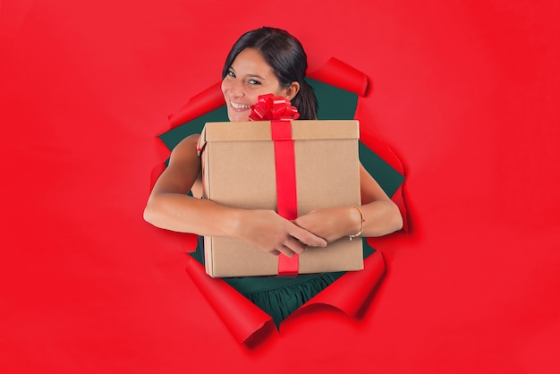 Woman inside a hole on a red paper backdrop holds tight in her arms a gift package