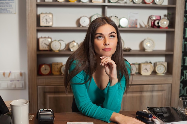 Woman is against background of shelves with clocks base herself upon the table