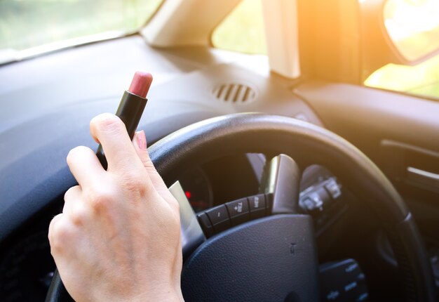 Woman is applying makeup in the car. Girl with lipstick behind the wheel. Dangerous situation on the road. Possibility of accident.