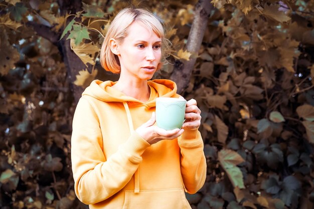 The woman is in the autumn park with cup of tea Autumn atmosphere