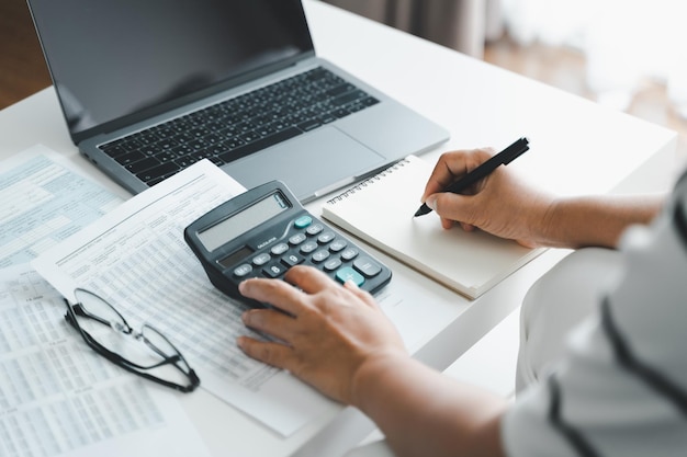 Woman is calculating annual tax, monthly expenses with calculator and filling form of Individual Income Tax Return. Season to pay Tax and Budget planning concept.