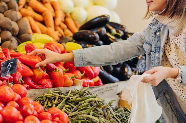 Woman is chooses fruits and vegetables at food market. Reusable eco bag for shopping. Sustainable lifestyle. Eco friendly concept.