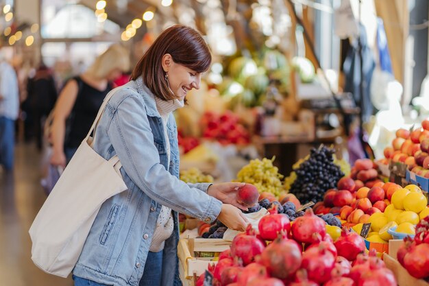 Женщина выбирает фрукты и овощи на продуктовом рынке. Многоразовая эко-сумка для покупок. Устойчивый образ жизни. Экологичная концепция.