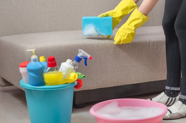Женщина убирает дом, квартиру, чистит диван губкой и пеной от моющего средства.