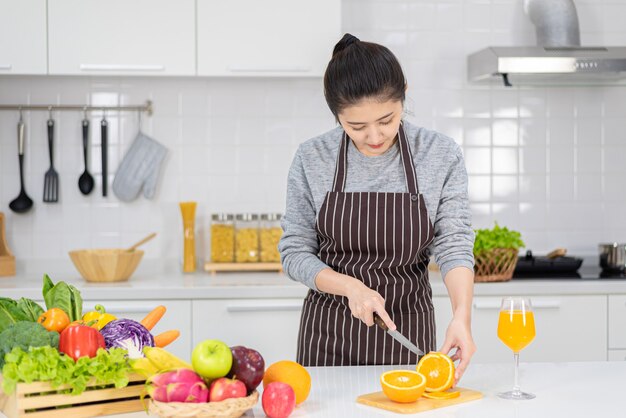 女性は家庭の台所で料理をしています。女性の手がテーブルの上で野菜を切ります。サラダと健康食品を作ることを学ぶ女性、家にいるコンセプト。