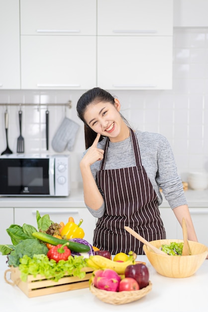 女性は家庭の台所で料理をしています。サラダと健康食品を作ることを学ぶ女性、家にいるコンセプト。