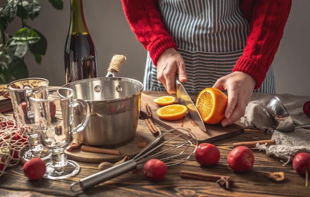 女性はグリューワインを作るためにナイフでオレンジを切っている 温かみのある伝統的な飲み物を居心地の良いお祝いの雰囲気にするプロセス