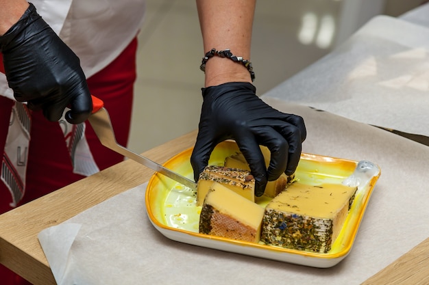 A woman is cutting pieces of cheese with a knife on a yellow plate for presentation