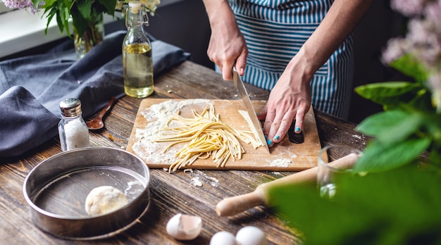 Foto una donna sta tagliando la pasta cruda con un coltello per fare le tagliatelle fatte in casa