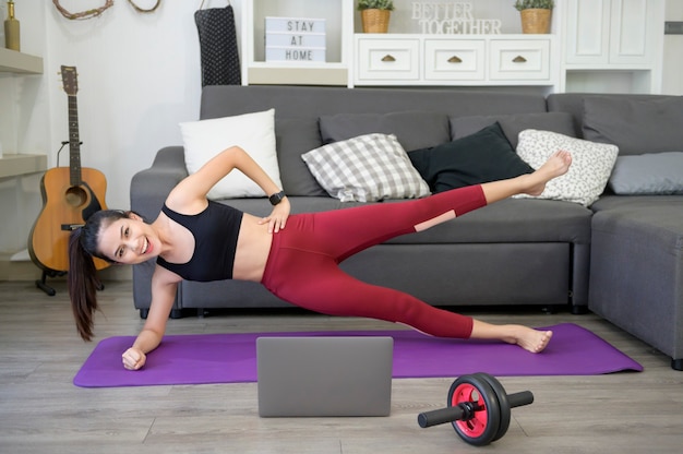 Una donna sta facendo yoga e guardando tutorial di formazione online sul suo laptop in salotto, allenamento fitness a casa, concetto di tecnologia sanitaria.