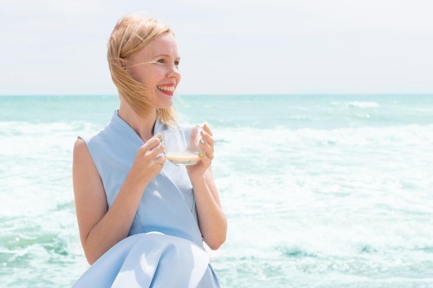 A woman is drinking tea with milk from a large cup on the ocean the sea