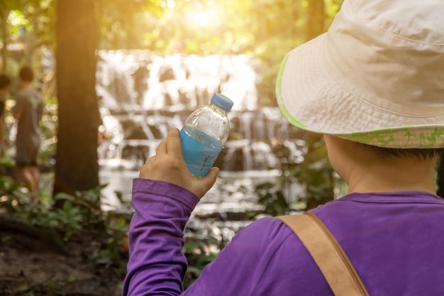 Photo a woman is drinking water from a water bottle a woman is thirsty while hiking in the forest travel