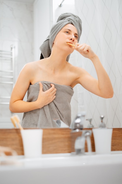 Woman is engaged in morning body care brushing her teeth in the bathroom in front of the mirror