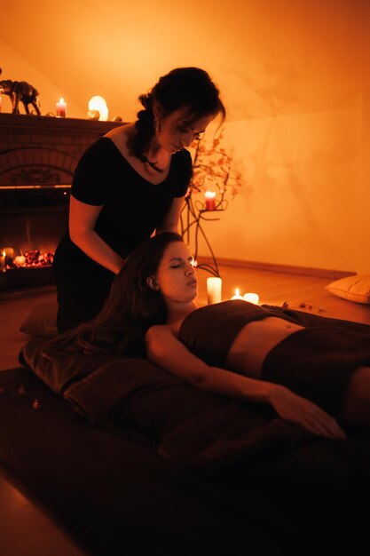 A woman is giving a massage to a woman in a room with a fireplace and a fire in the background.