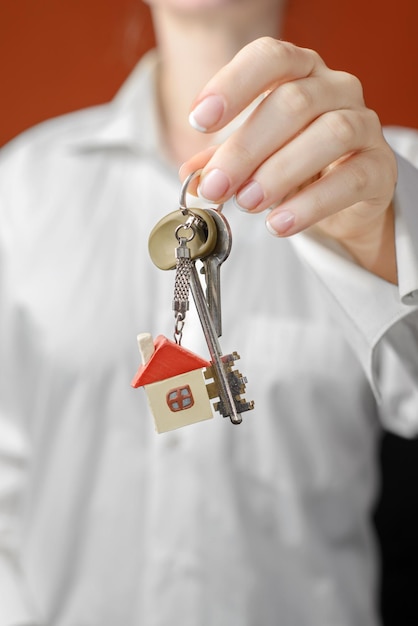 Photo woman is handing a house key key with a keychain in the shape of the house on a orange background