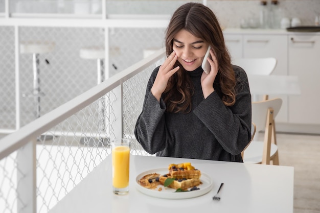 A woman is having breakfast with belgian waffles and orange juice