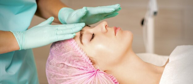 The woman is having cosmetic treatment during cosmetologist in medical gloves are touching the female face at the spa salon.