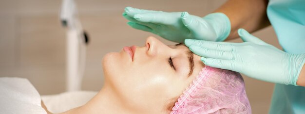 The woman is having cosmetic treatment during cosmetologist in medical gloves are touching the female face at the spa salon.