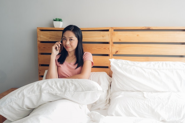 Woman is having a phone conversation on her bed in the morning.